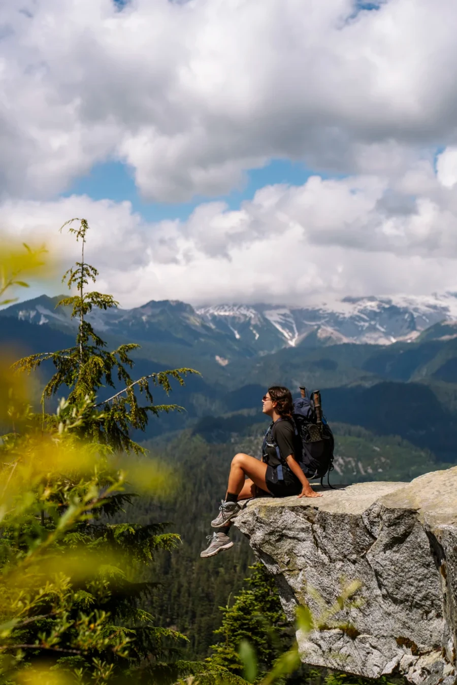 Woman sits on a rock that hangs over a massive cliff looking out to distant mountains