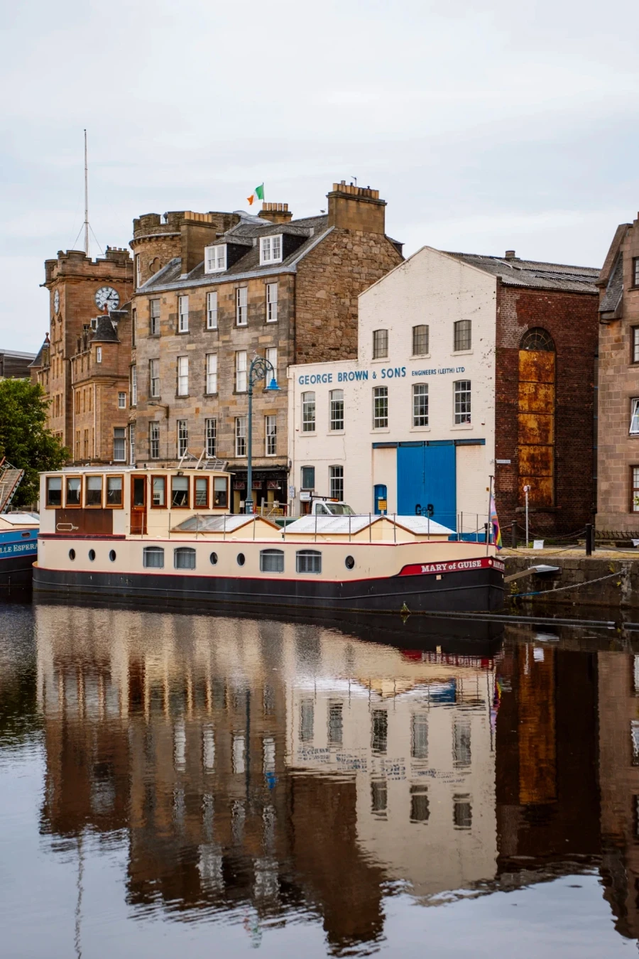 Old town buildings are reflected perfectly in the canal with a houseboat docked in Leith, Edinburgh