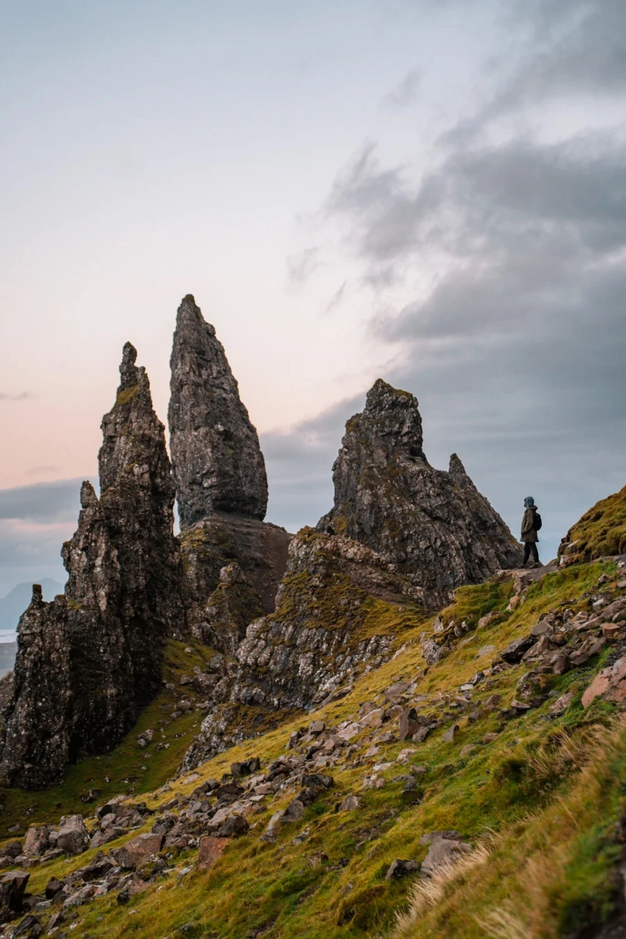 A man standing in the distance made to look small next to the massive stone pillars of the Old Man of Storr
