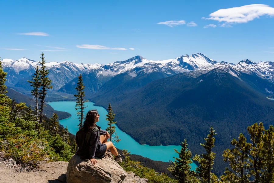 A woman sitting on a boulder in the Whistler alpine with the Cheakamus Lake visible in the valley below