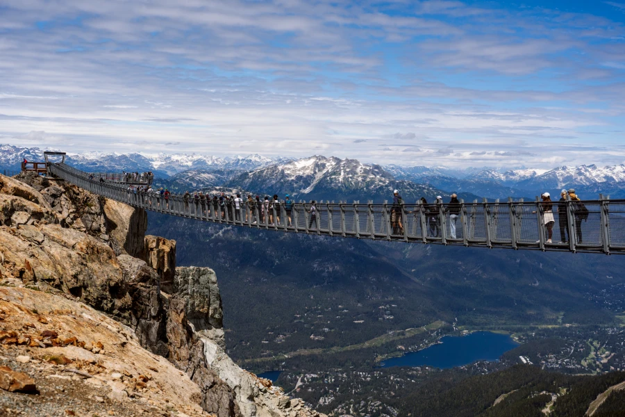 Several tourists walk across a huge metal suspension bridge at the peak of Whistler Mountain