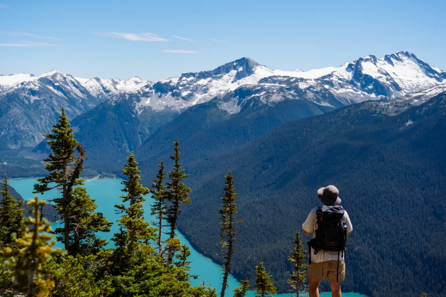 A man stands on the edge of a cliff in the Whistler alpine looking out at the snow-capped peaks that tower over Cheakamus Lake