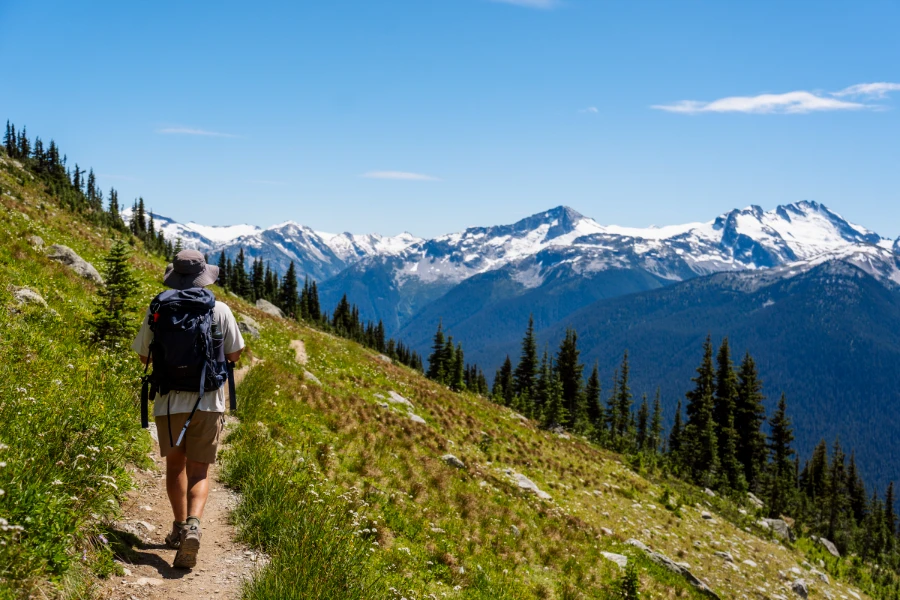 A man walks along a narrow dirt path that is a part of the High Note Trail in the Whistler alpine