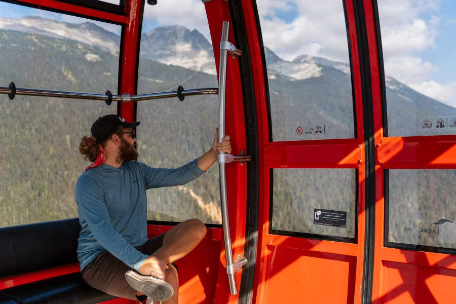 Man site inside a red gondola looking out at the view of the valley below while riding across the Peak 2 Peak in Whistler, BC