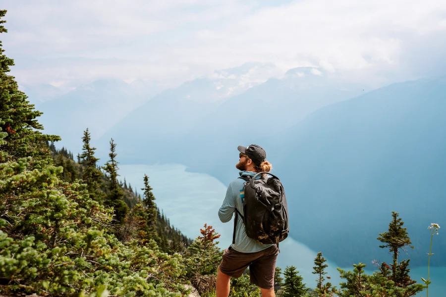 A man with a backpack looks out the the view of a blue lake in the valley below