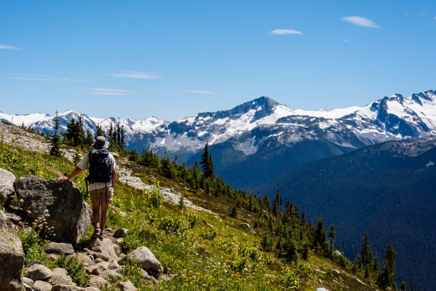 A man with a wide-brimmed hat and a large backpack hiking in the Whistler alpine