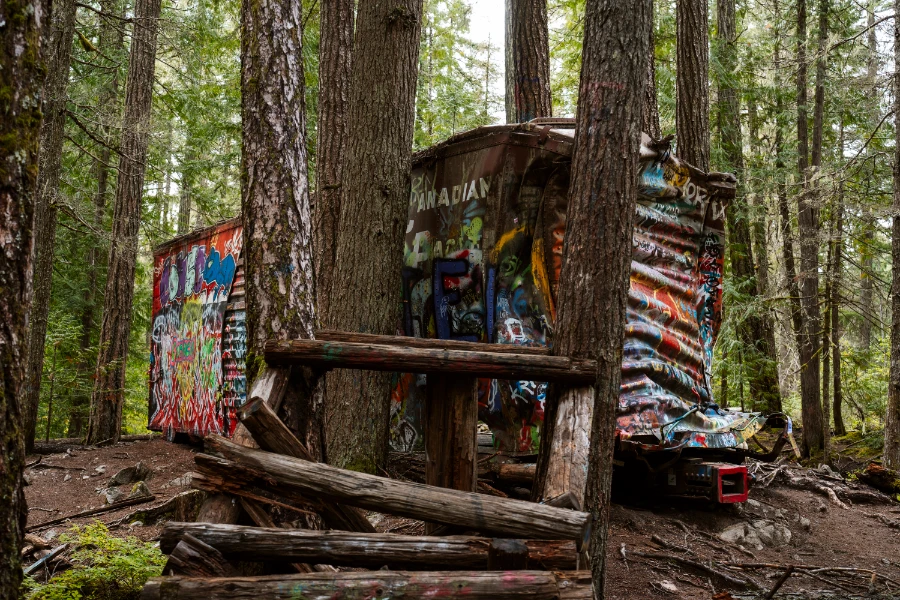 A decrepit old bike jump landing sits in ruins in front of an abandoned and rusty rail box-car covered in graffiti