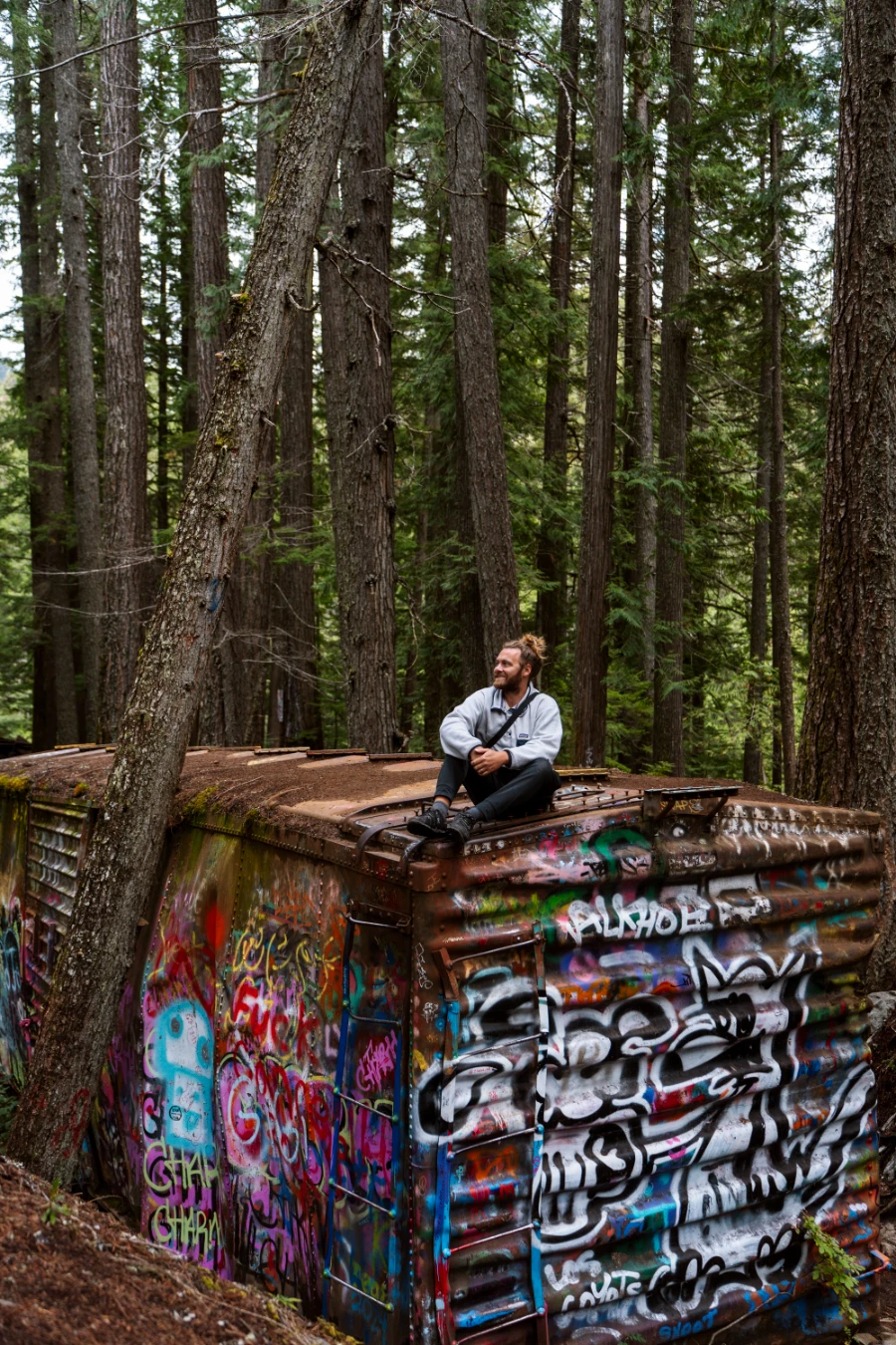 A man sitting on top of an abandoned and rusty rail box-car covered in graffiti