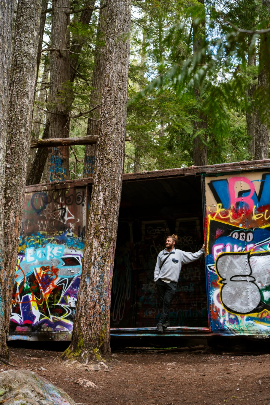 A man standing inside an abandoned and rusty rail box-car covered in graffiti